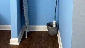 A corner of a room with blue walls, a white shelf, a mop, and a broom. - SM50 Bright Studio walk to the beach (Myrtle Beach)