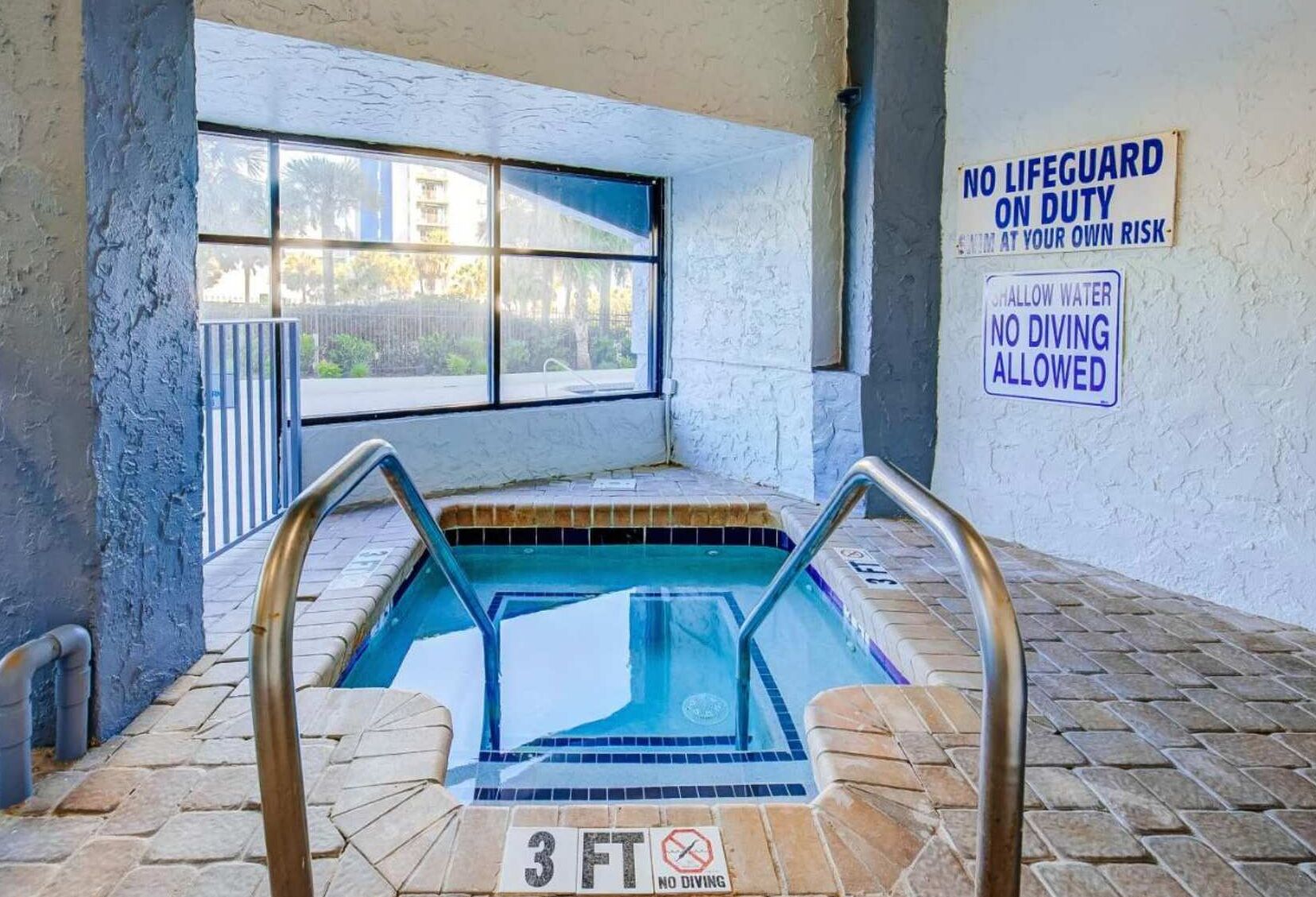 Una piscina interior amb un senyal que indica una profunditat de 3 peus, senyals de seguretat i una vista per una finestra.