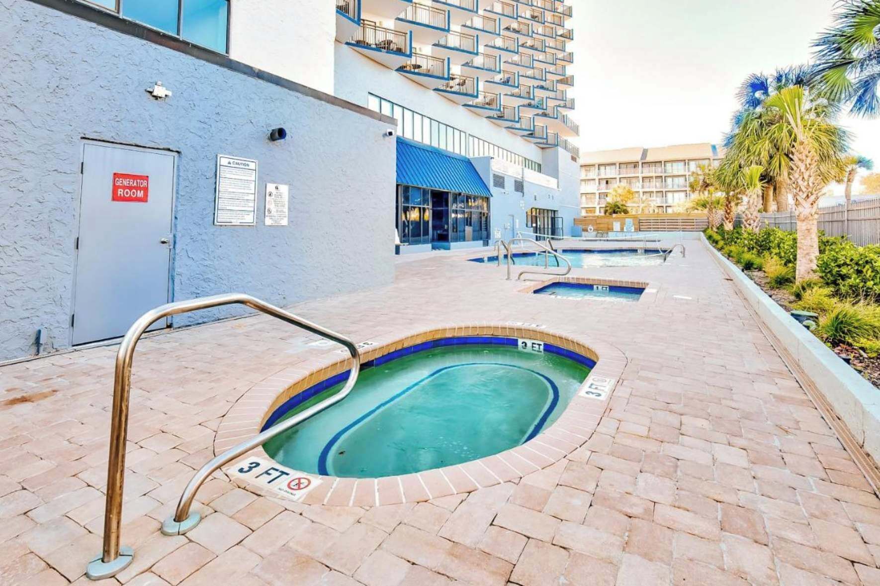 A pool area with a sign indicating a generator room, a pool with a 3 FT depth marker, and a building with balconies in the background.