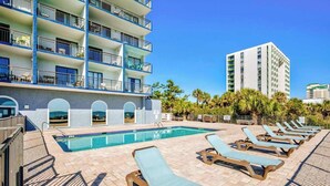 A pool area with lounge chairs, a clear pool, and a building with multiple balconies. - Blue Water Resort #19 great studio on the beach! (Myrtle Beach)