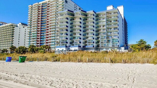 A multi-story hotel with balconies, located near a beach with sand and sparse vegetation. - Blue Water Resort #19 great studio on the beach! (Myrtle Beach)