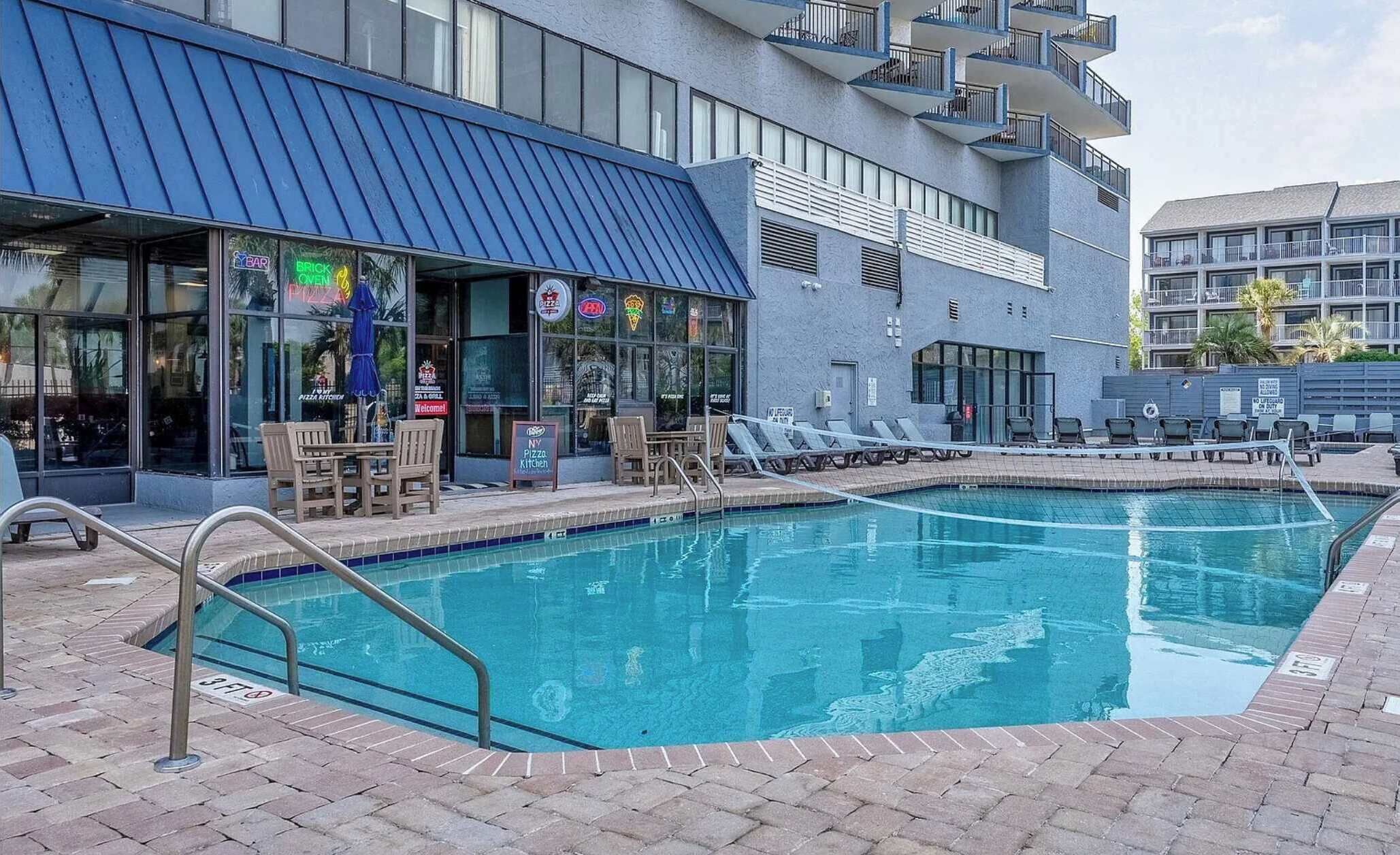 A pool area with a restaurant named 'Brick Oven Pizza Kitchen' adjacent to it.
