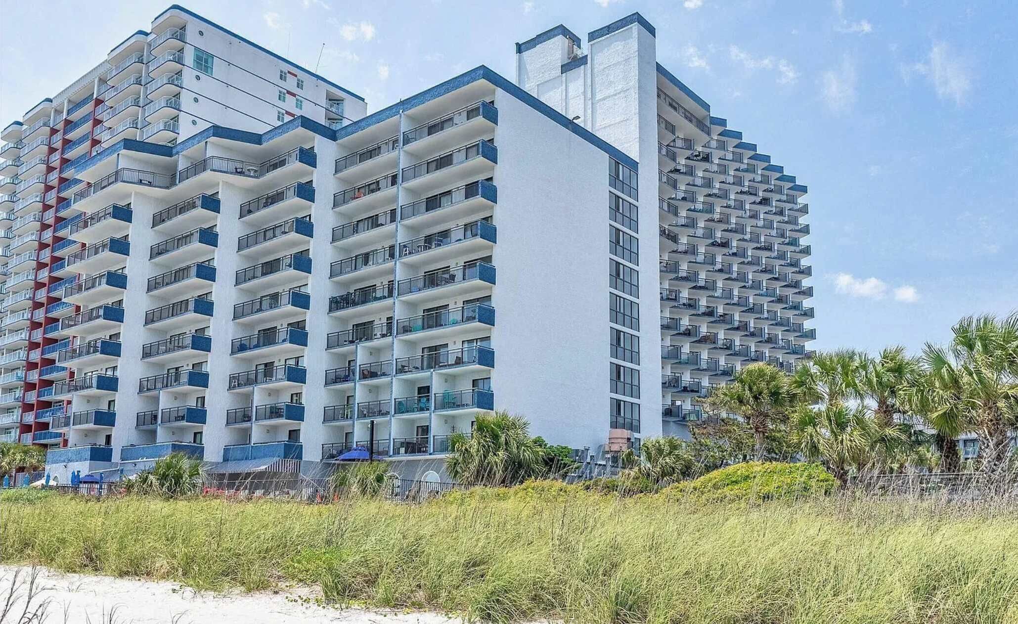 Un hotel de gran altura con múltiples balcones, techo plano y ubicación frente a la playa.