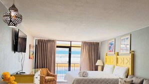 Camera d'albergo con un letto, un divano, una scrivania, una sedia, una TV e un balcone con tende.