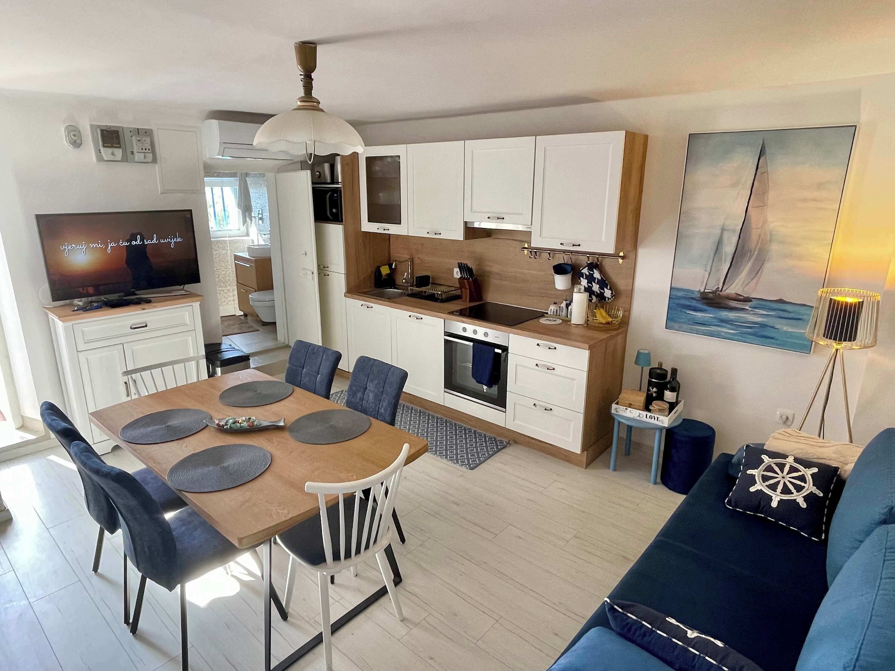 Una cocina moderna con armarios blancos, horno empotrado y comedor con mesa y sillas de madera.