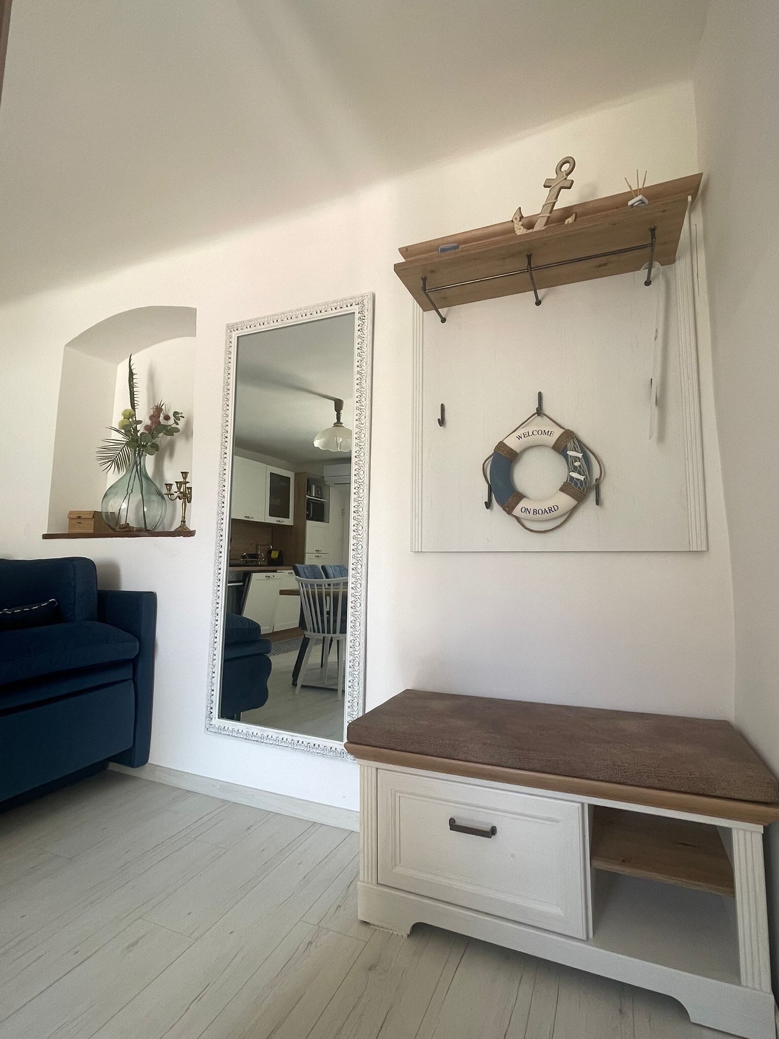A room with a large mirror, a wooden bench, a wall-mounted shelf, and a welcome sign.