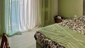 Une chambre à coucher comprenant un lit, une chaise, une fenêtre avec des rideaux légers et un appareil de climatisation.