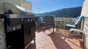 Une terrasse avec un barbecue, des chaises longues et une vue sur les montagnes.