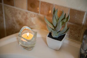 A small glass candle holder with a lit candle and a potted succulent plant on a bathroom counter. - Xuru Stays I Play Foosball & Do Yoga - 1 BR Apt. 5 Min To Airport (Cairo)