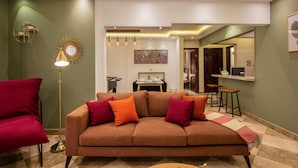 A modern living room with a sofa, red chair, floor lamp, and a dining area in the background. - Xuru Stays I Play Foosball & Do Yoga - 1 BR Apt. 5 Min To Airport (Cairo)