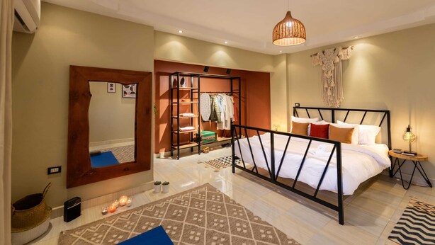 A bedroom with a bed, bedside table, lamp, and a wardrobe. - Xuru Stays I Play Foosball & Do Yoga - 1 BR Apt. 5 Min To Airport (Cairo)