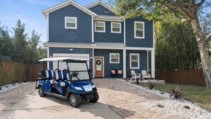 A two-story house with a driveway, a golf cart, and a front porch with chairs.