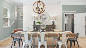A dining room with a large wooden table, white chairs, and a chandelier.