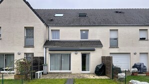 A two-story residential building with a flat roof, a covered front porch, and a small front yard with a pathway. - Charming, cosy room just 5 minutes from Lille (Marcq-en-Barœul)