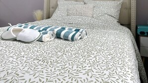 A neatly made bed with a leaf-patterned bedspread, a rolled-up towel, and slippers. - Charming, cosy room just 5 minutes from Lille (Marcq-en-Barœul)