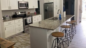 A modern kitchen with white cabinets, stainless steel appliances, granite countertops, and bar stools.