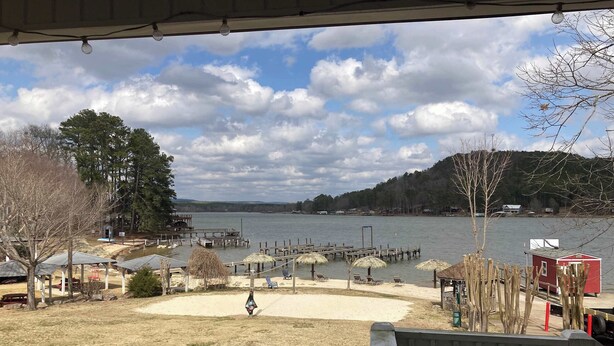 A lakeside view with a dock, umbrellas, and a red building.