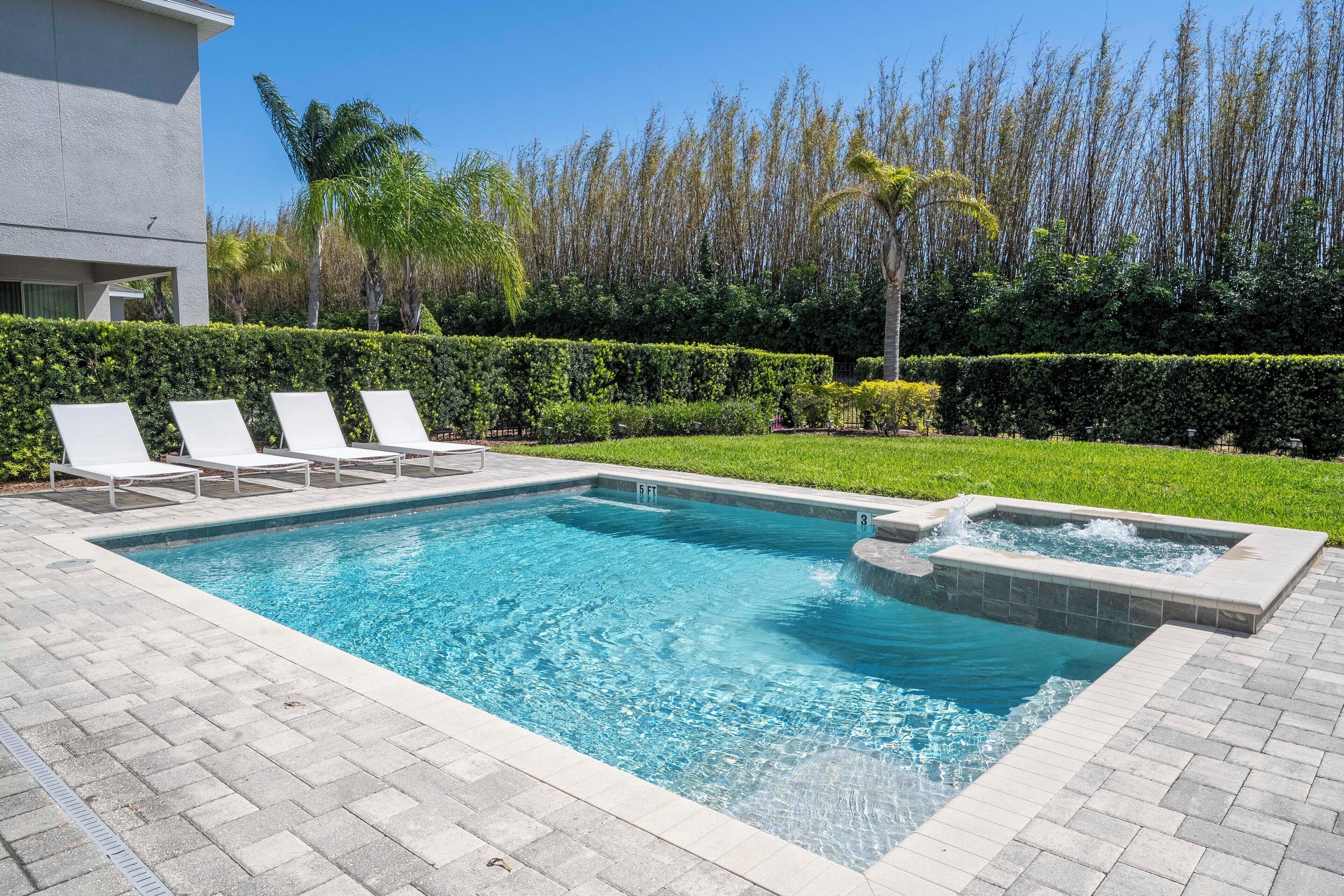 Una piscina rectangular con un jacuzzi, rodeada por una solana empedrada y sillas de descanso blancas.