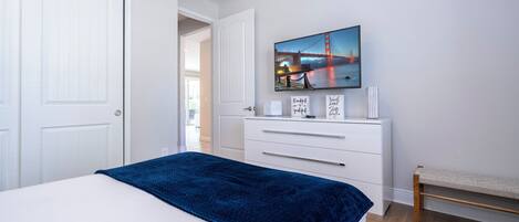 A bedroom with a bed, a dresser, a bench, and a painting of a bridge.