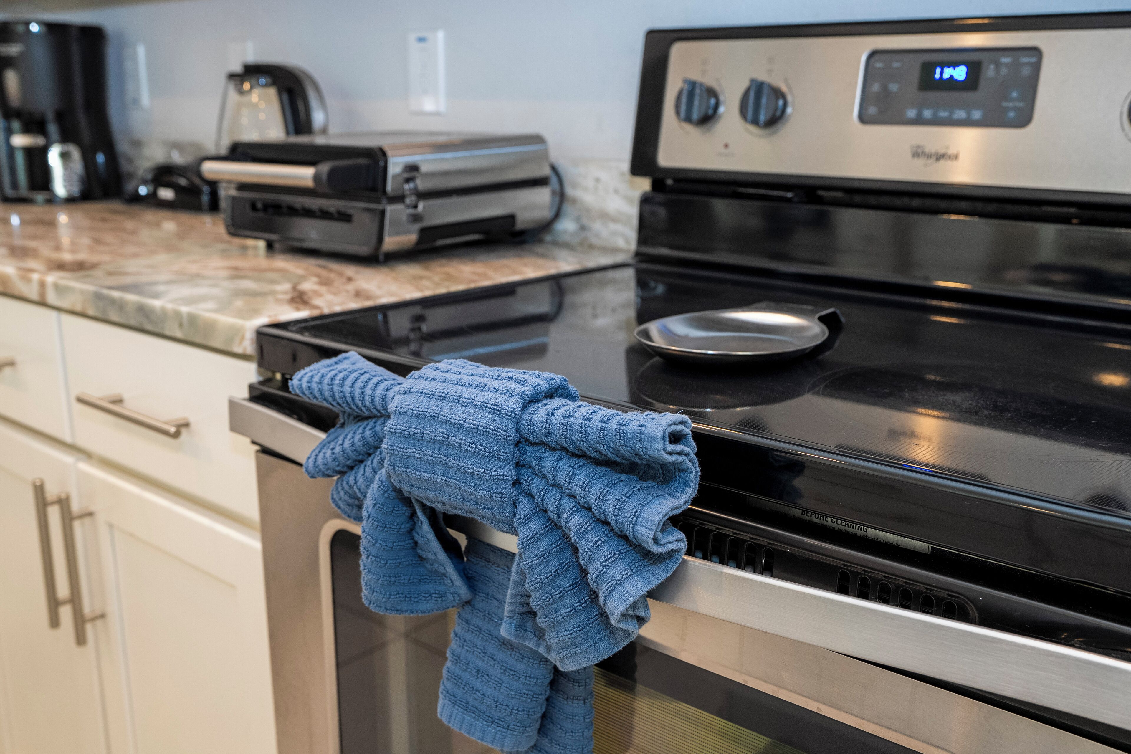 A kitchen with a stainless steel stove, a digital clock, and a countertop with a coffee maker and toaster.