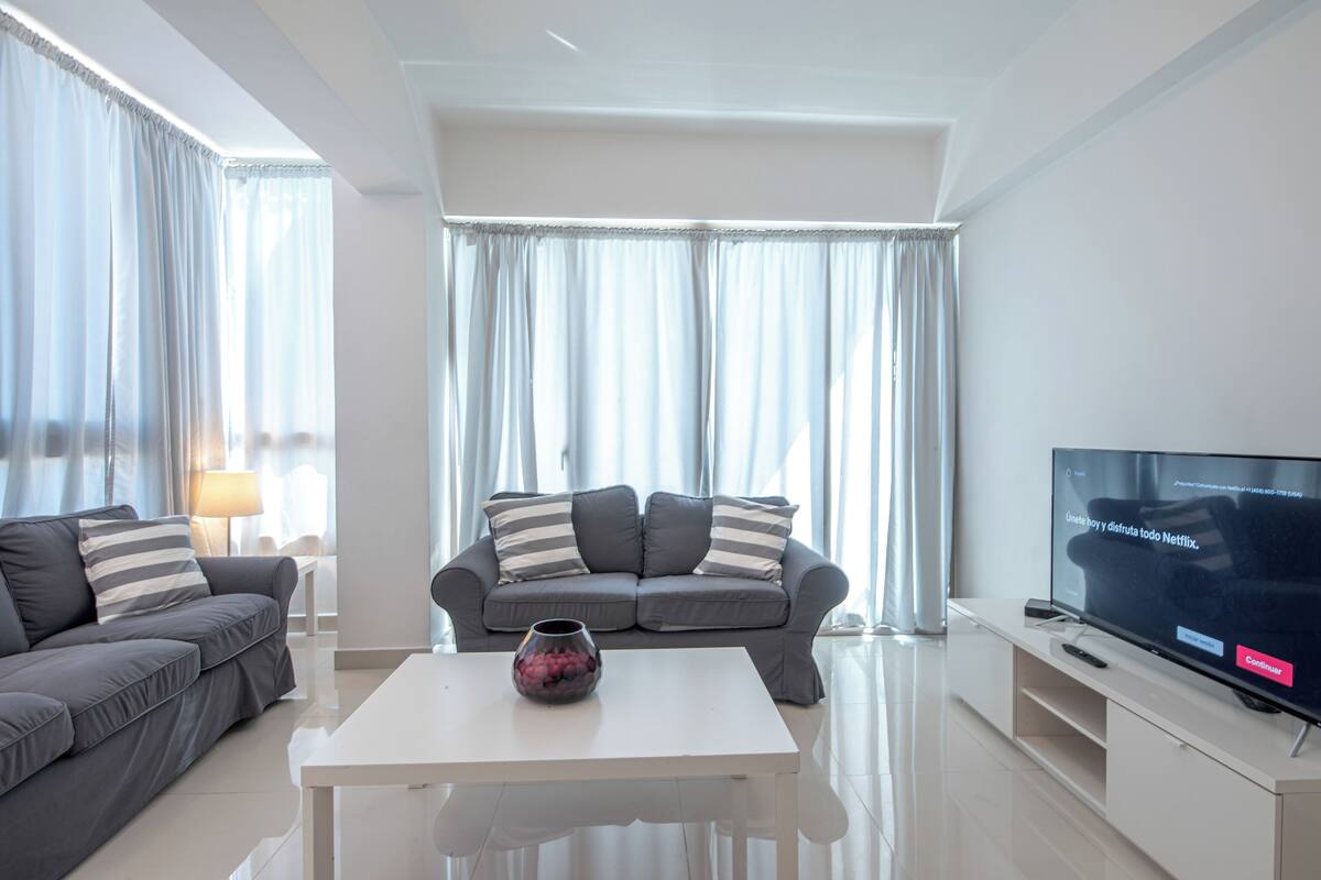 Una sala de estar moderna con un sofá gris, una mesa de centro blanca y un televisor de pantalla plana.