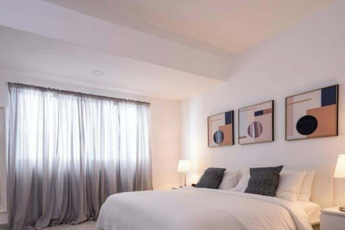 Habitación de hotel con una cama, dos mesitas de noche con lámparas, un televisor en una cómoda y tres cuadros en la pared.