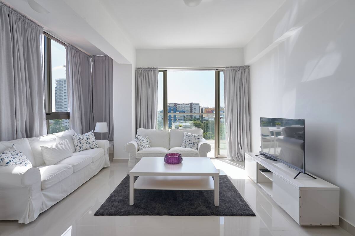 Una sala de estar moderna con un sofá blanco, una mesa de centro y un televisor sobre un mueble.
