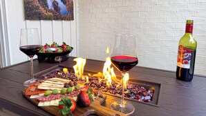 Una mesa con una tabla de fiambres, dos copas de vino tinto, una botella de vino y un bol de fresas.