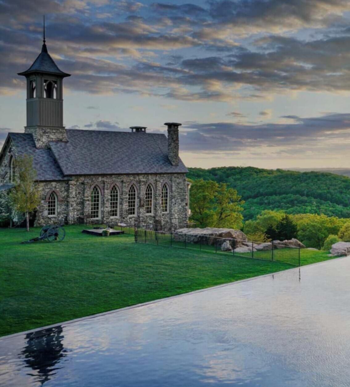 A stone church with a bell tower, surrounded by a grassy area and a body of water.