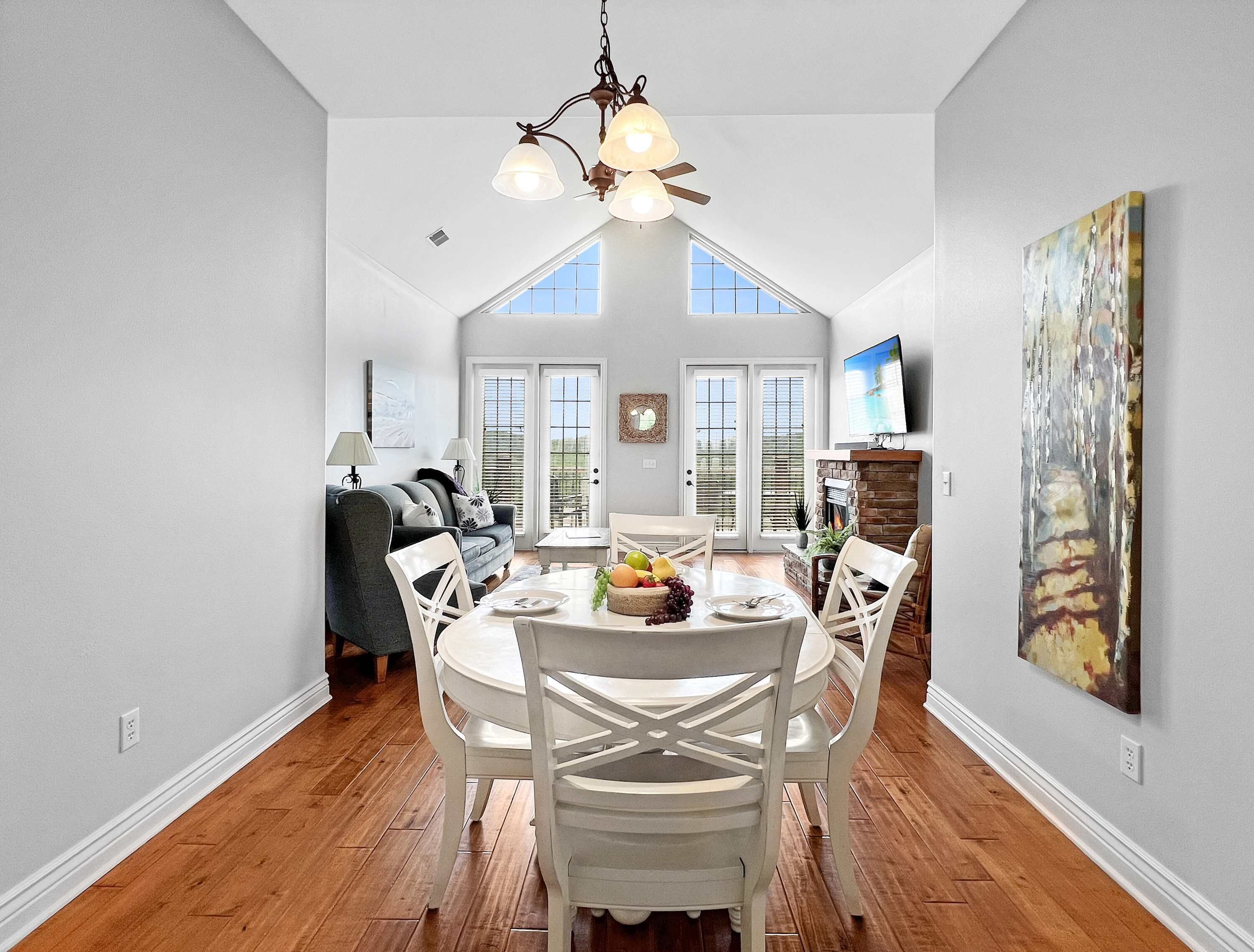A dining area with a high ceiling, a chandelier, and a view through the windows.