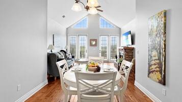 A dining area with a high ceiling, a chandelier, and a view through the windows.