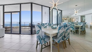 A modern dining area with a large table and chairs, a ceiling fan, and a view of the ocean through large glass doors. - 2-Level Beachfront Resort Condo w/Views of Beach & Bay! (South Padre Island)