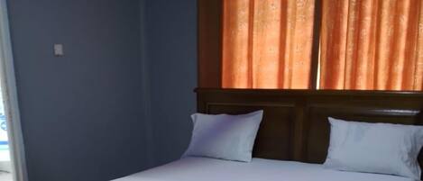 Un dormitorio con estructura de cama de madera, ropa de cama blanca y alfombra estampada con flores.