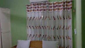 Une chambre à coucher comprenant un lit, un ventilateur de plafond, un appareil de climatisation et un rideau à motifs à pois.