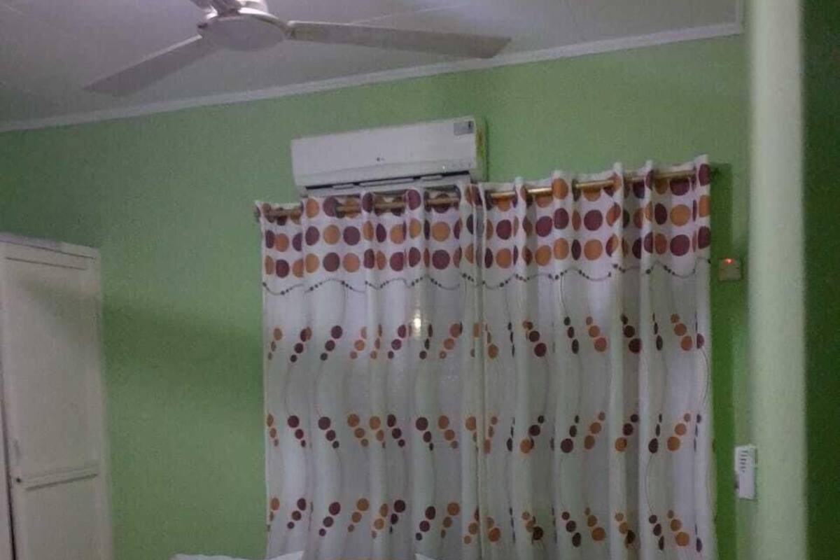 A bedroom with a bed, a ceiling fan, an air conditioning unit, and a curtain with a polka dot pattern.