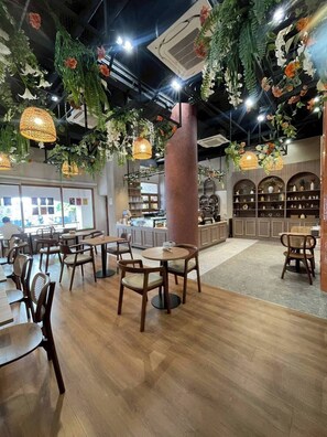 Ein Restaurant mit Holztischen und -stühlen, hängenden Pflanzen und Pendelleuchten.
