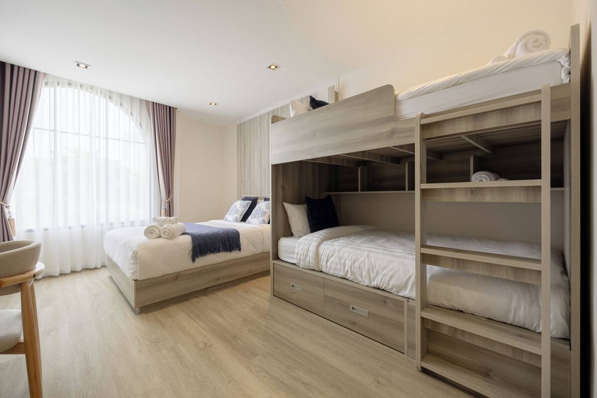 Quarto moderno com beliche, mesa de cabeceira e uma janela grande com cortinas.