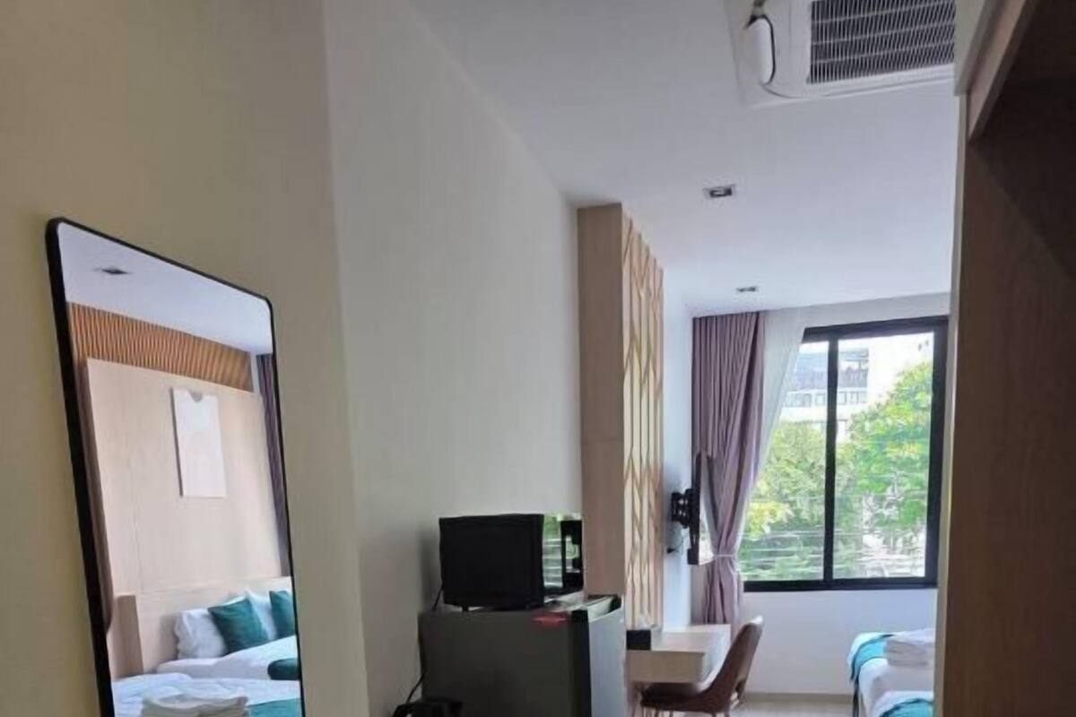 Quarto de hotel com uma cama, uma escrivaninha, uma cadeira, uma televisão e uma janela.