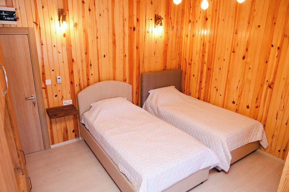 Una habitación pequeña con paneles de madera, dos camas individuales, un armario de madera y lámparas fijadas a la pared.