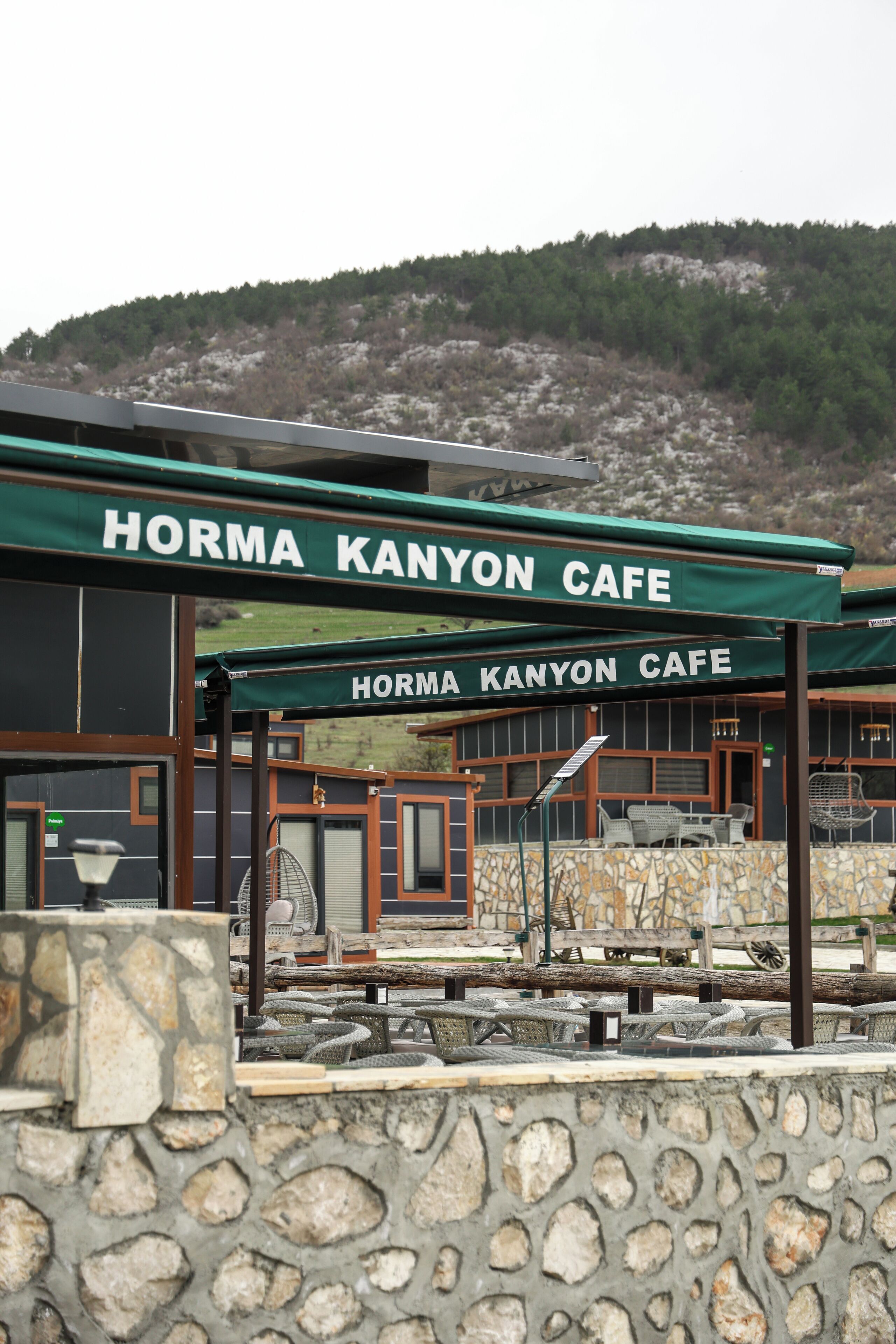 Café con mesas al aire libre y un muro de piedra al frente.