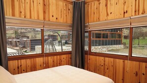 A bedroom with wooden walls, a bed, and large windows overlooking a garden and outdoor area. - Horma Kanyon Otel (Pinarbasi)