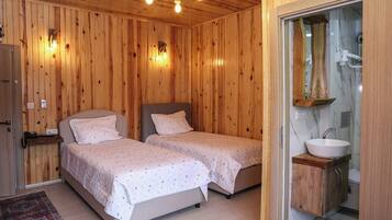 A wooden-paneled room with two beds, a bedside table with a phone, and a bathroom with a sink and mirror.