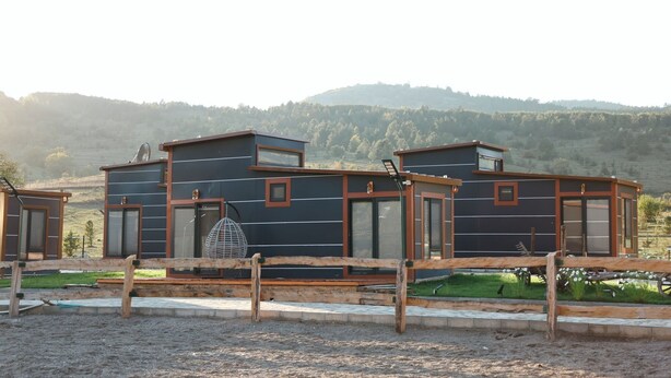 A modern, multi-story building with large windows and a flat roof, surrounded by a wooden fence and a gravel area. - Horma Kanyon Otel (Pinarbasi)