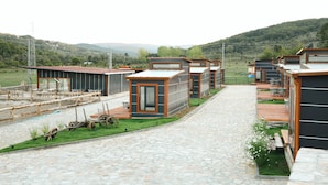 A row of modern, compact cabins with a stone-paved pathway leading to a communal area with outdoor seating and a bicycle. - Horma Kanyon Otel (Pinarbasi)