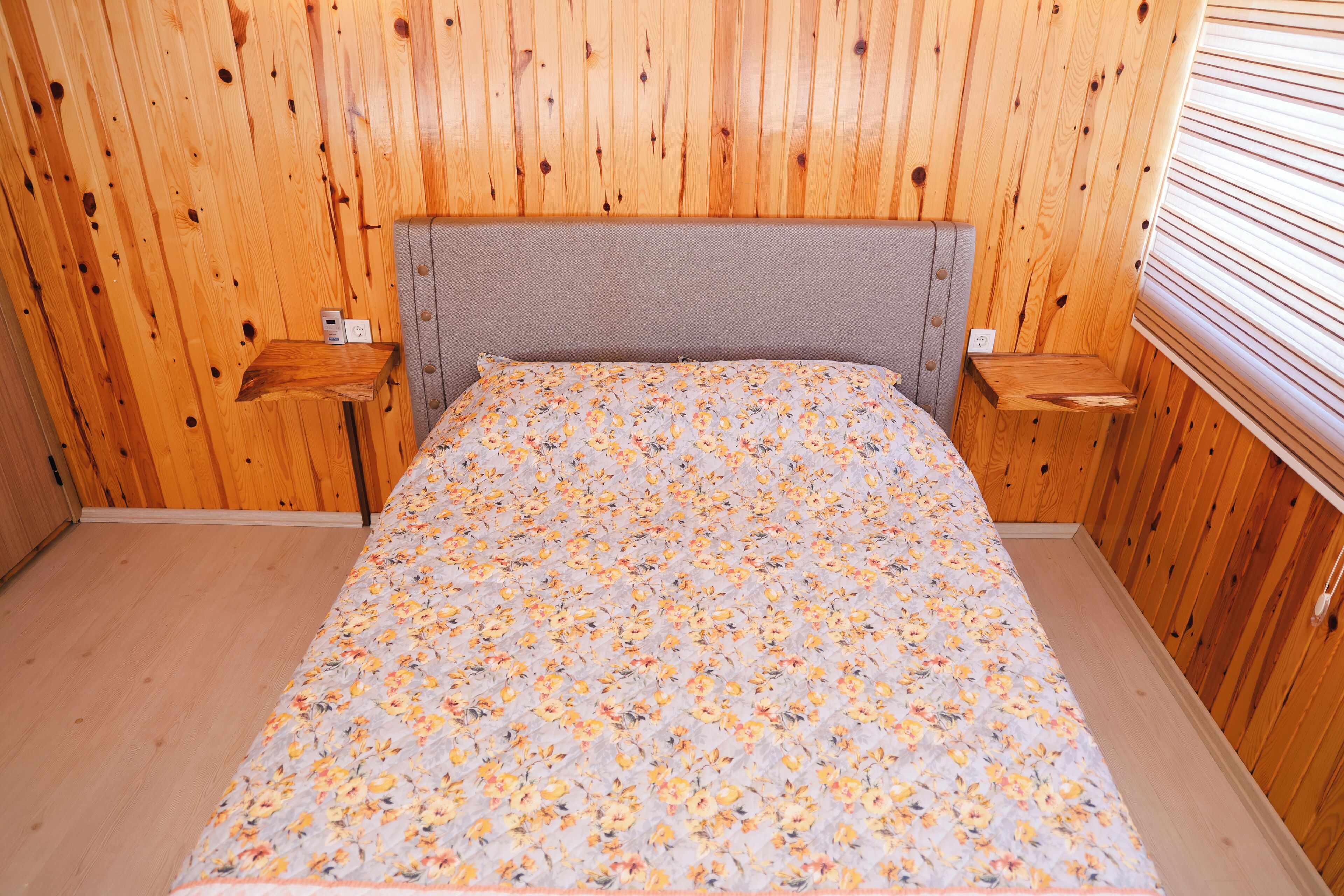 A wooden-paneled room with a bed, two nightstands, and a window with blinds.