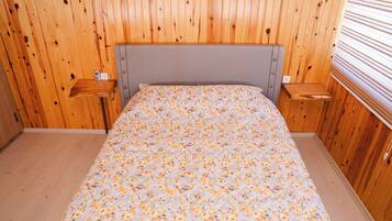 A wooden-paneled room with a bed, two nightstands, and a window with blinds.