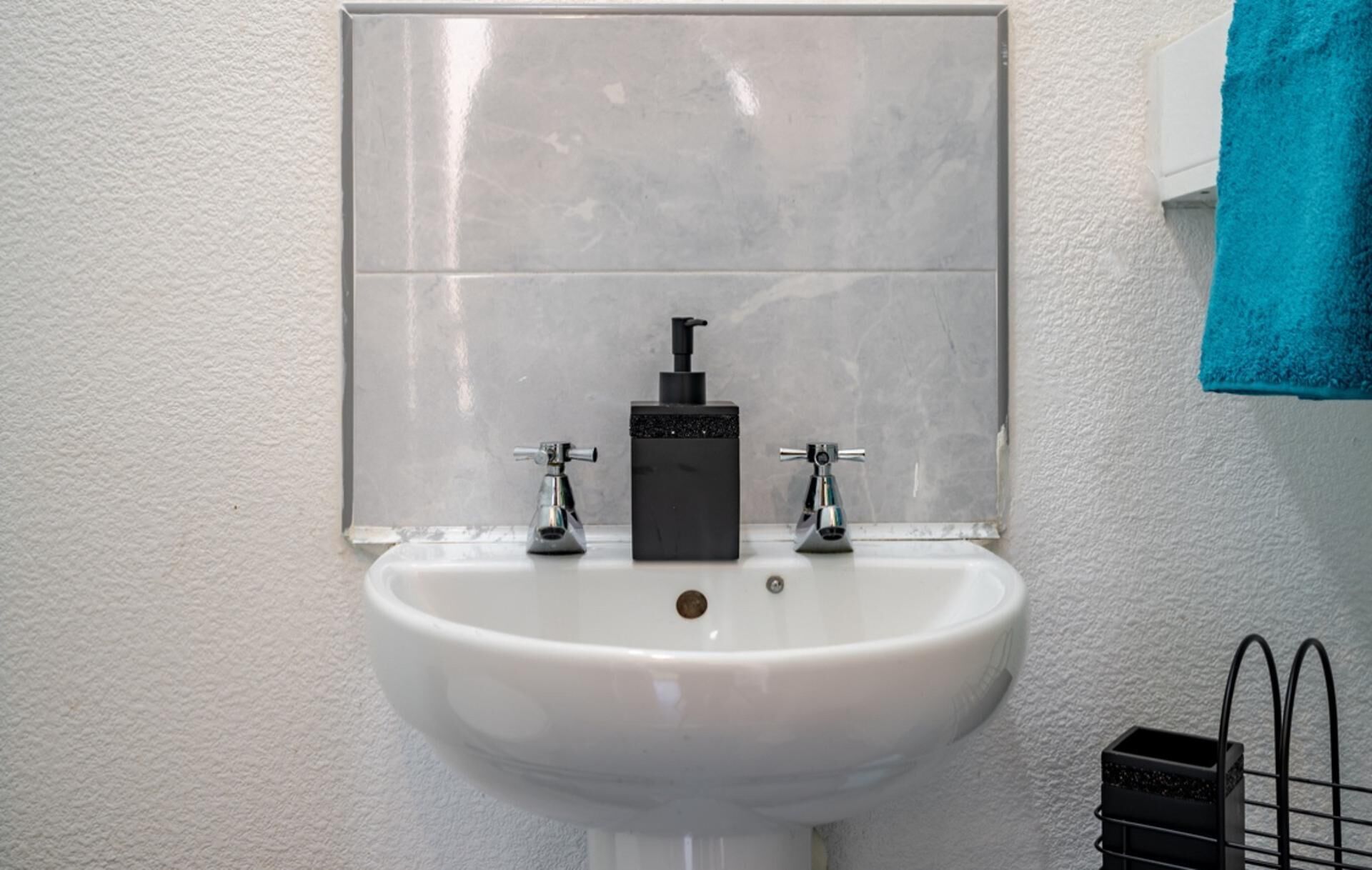 A bathroom with a white sink, two faucets, and a black soap dispenser.