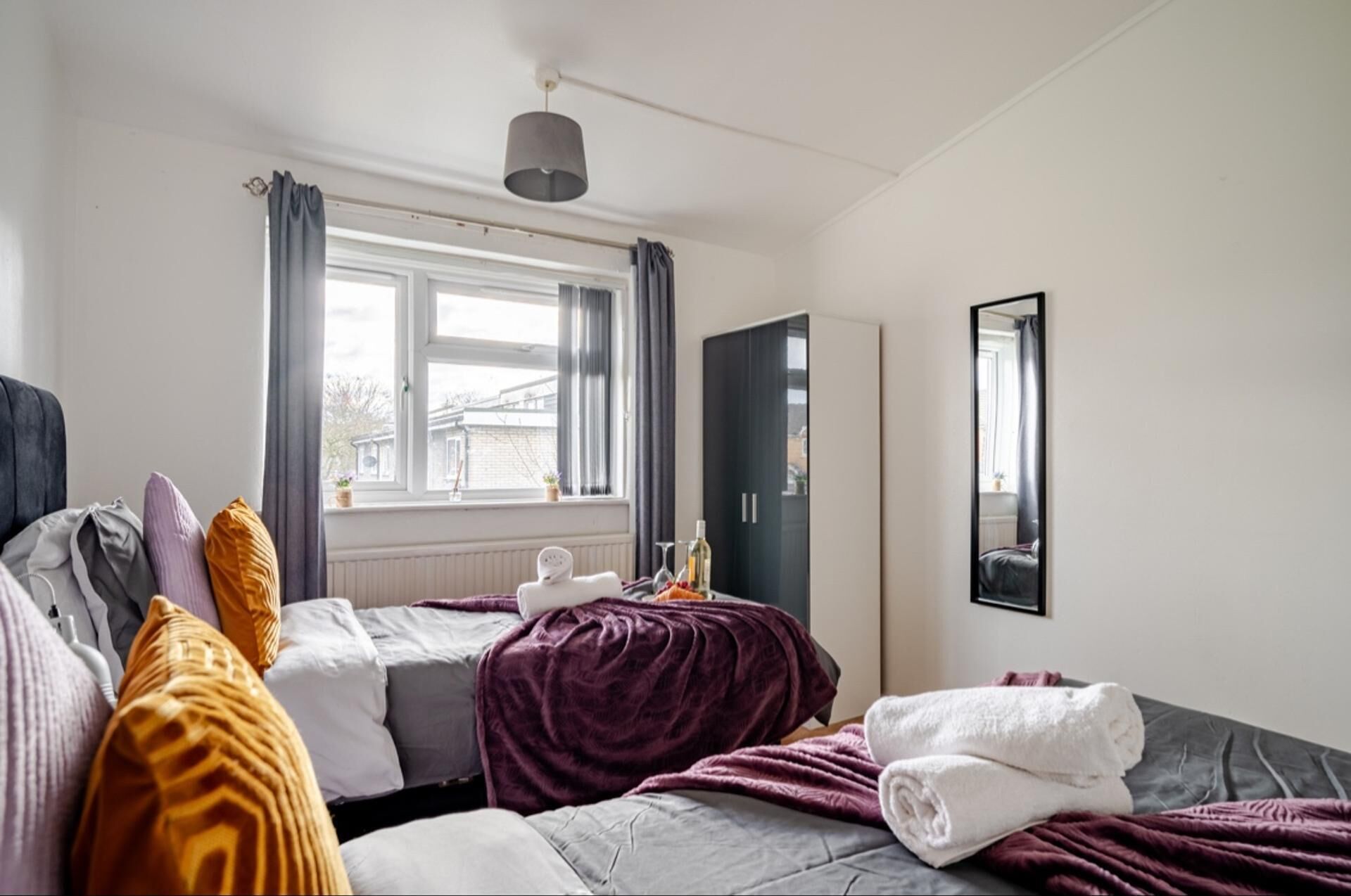 A modern bedroom with a bed, a wardrobe, a window with curtains, and a mirror on the wall.