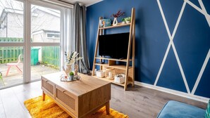 A living room with a wooden coffee table, a TV on a wooden stand, and a blue wall with white geometric patterns. - Hillside Haven in Manchester (Manchester)