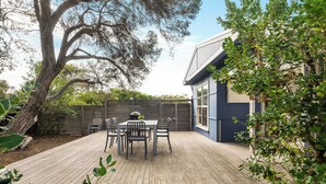 Una terraza con mobiliario exterior, una parrilla y un árbol grande.
